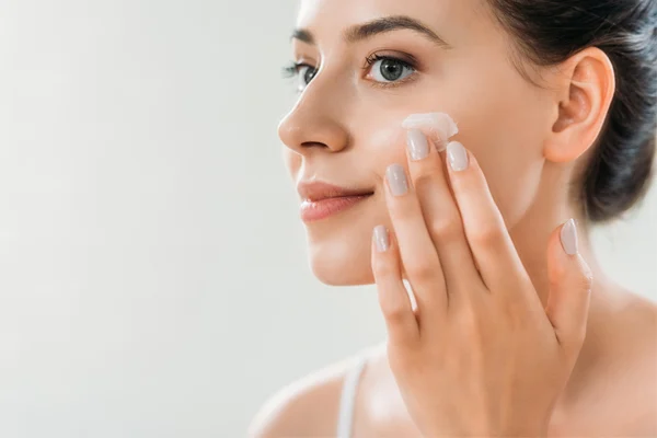 Uśmiechnięta kobieta z cerą pokrytą piegami nakłada krem na twarz.